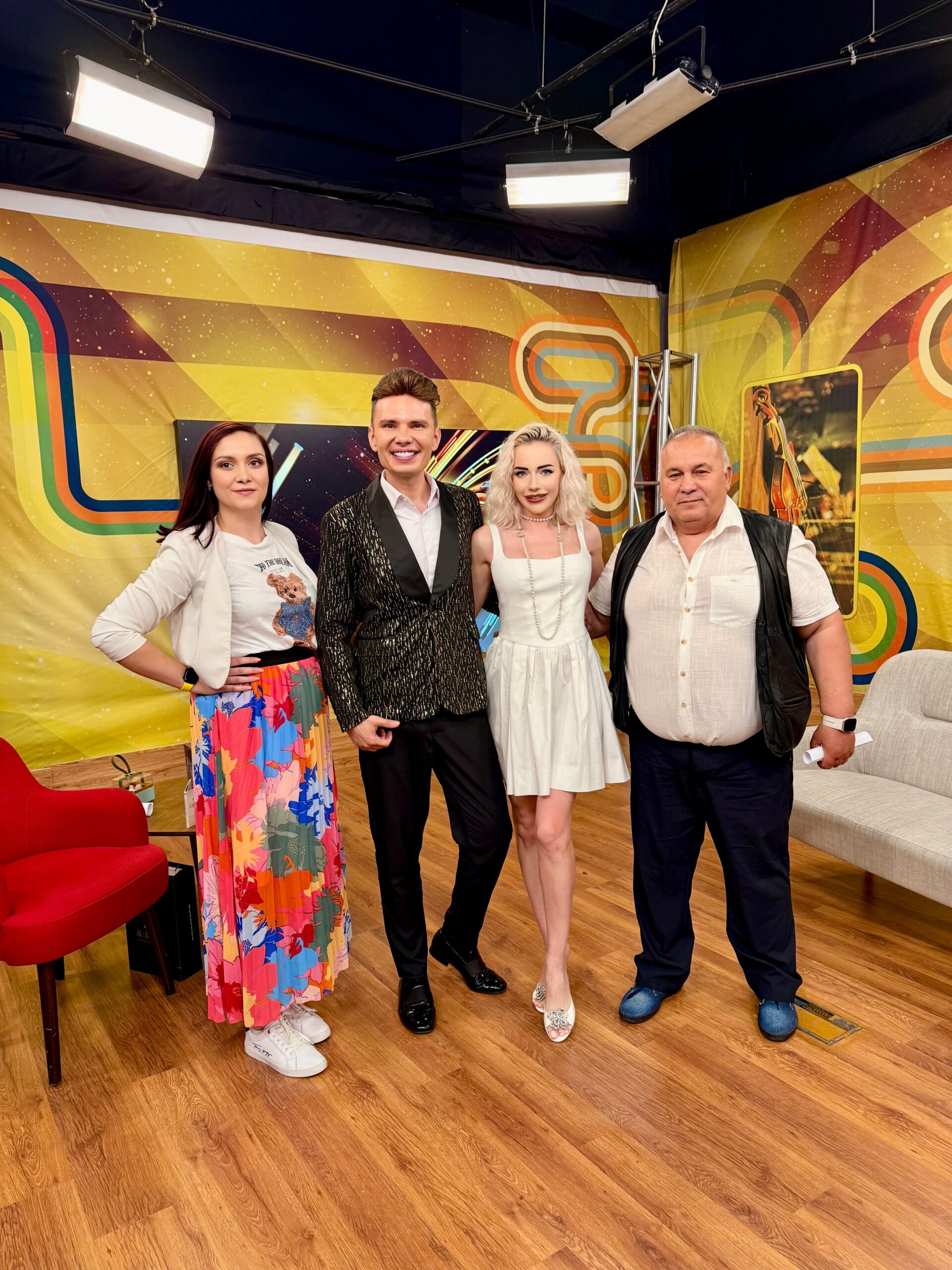 Four people pose together in a colorful studio with geometric yellow backdrop and bright lighting.